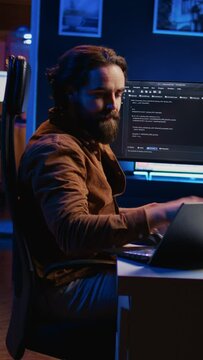Developer writing lines of code on multimonitor PC setup during remote job shift. IT expert doing multitasking in neon lit home office, listening music, drinking coffee, camera B