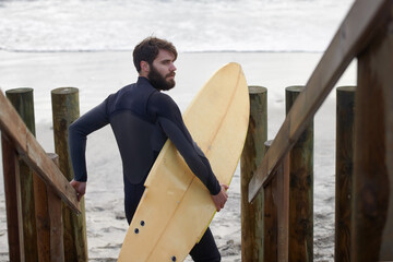 Man, surfer and beach by waves in fitness, exercise or extreme sports on outdoor shore. Rear view of male person or athlete with surfboard for surfing challenge or hobby at ocean coast, sea or nature