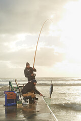 Fishing, men and net with fish at pier with rod, waves and relax on vacation, holiday and...