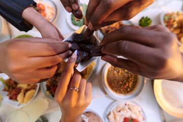 In a poignant close-up, the diverse hands of a Muslim family delicately grasp fresh dates, symbolizing the breaking of the fast during the holy month of Ramadan, capturing a moment of cultural unity
