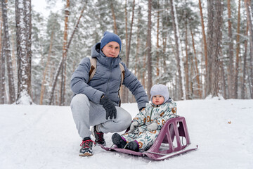 Fototapeta na wymiar A father and a small child on a sledge in a snowy pine forest in winter