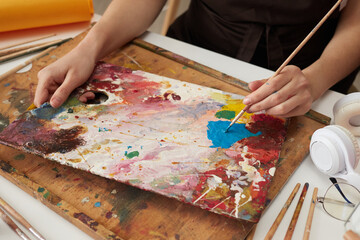Unrecognizable woman painter wearing brown apron in art studio drawing picture using colorful paints drawing abstract work of art closeup hands with paintbrush