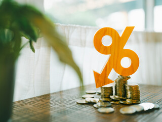 A percentage symbol made of wood and an arrow, a graph pointing down and a pile of coins on a table are images with the idea of a policy to reduce interest rates on deposits and loans.
