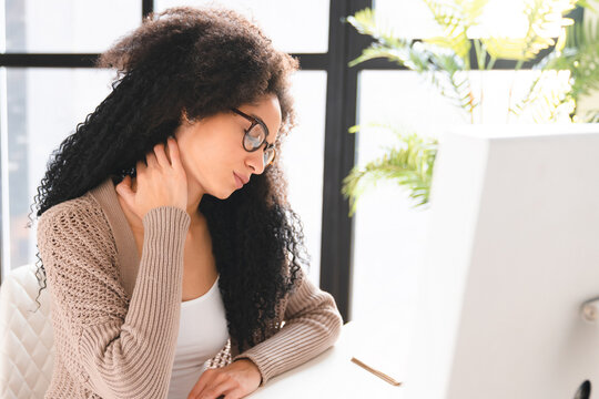Young african woman business lady freelancer tutor having neck pain ache, rubbing her back after overworking, multitasking, depressed on workplace, leading sedentary lifestyle