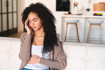 Young african woman having stomach ache, period crumps, feeling sad and depressed, suffering from...