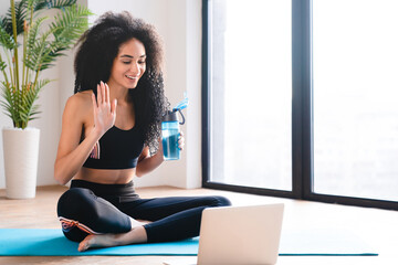 Young female athlete african sportswoman in fitness clothes having online lesson, trainer talking to subscribers, broadcasting workout, yoga using laptop at home