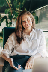 Testimonial portrait of a business woman sitting in a chair in the office with a mobile phone.