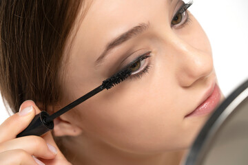 Portrait of a young woman applying mascara with brush on a white background