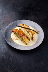 Traditioneller bayerischer Apfelstrudel mit gebackenen Äpfeln, Rosinen und Vanillesoße serviert als Nahaufnahme auf einem Design Teller