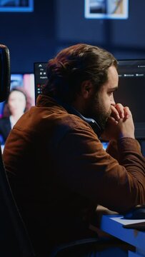 Technician focused on typing complex code in neon lit home office, developing software application. It specialist removing headphones to better concentrate on difficult task, camera A