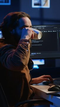 Software programmer putting headphones on while developing code, making time pass faster during remote job shift. IT professional doing multitasking in apartment office while listening music, camera A