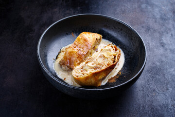 Traditioneller bayerischer Apfelstrudel mit gebackenen Äpfeln, Rosinen und Vanillesoße serviert als Nahaufnahme auf einem Design Schale