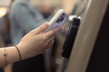 Close-up of a woman paying at a self-service machine using a contactless phone payment, Woman using the ticketing system by cellphone with NFC technology