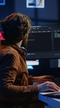Technician typing code in neon lit personal office, using javascript programming language to develop software application. It specialist using multimonitor desktop setup to finish project, camera A