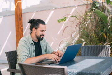 A male freelancer, a digital nomad, remotely works on a laptop in the hotel garden.