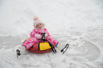 A little girl of 5 years old sits on a tubing and relaxes after skating on white figure skates at the skating rink in winter.