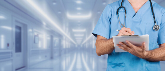 A focused male nurse in blue scrubs is using a tablet to record medical data