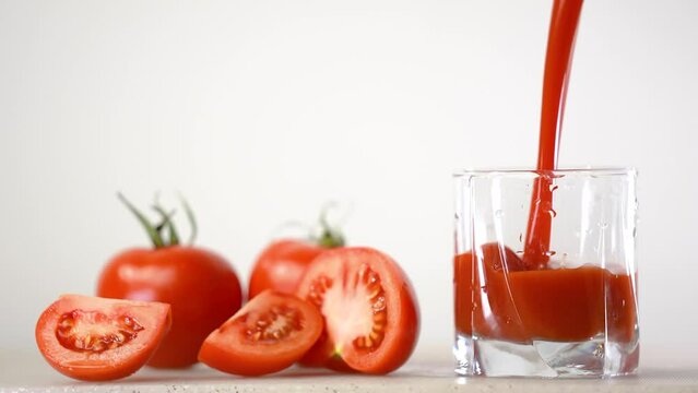 Delicious tomato juice is poured in jug next to tomatoes on the background 