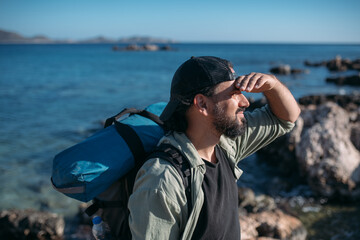 A male tourist with a large backpack and hiking gear on a rocky seashore.