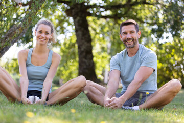 healthy couple stretching legs on the grass in the park