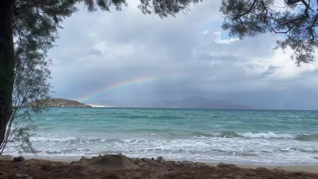 A beach with a rainbow and a stormy sky. Rainbow over the stormy sea after rain with lightning, calm sea in the foreground, Beach cove with dramatic clouds forming a rainbow over the blue ocean