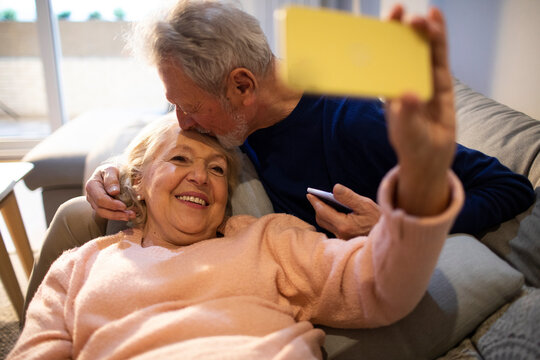 Happy senior couple relaxing on the couch with smartphone