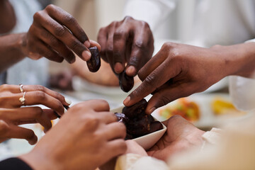 In a poignant close-up, the diverse hands of a Muslim family delicately grasp fresh dates,...
