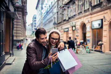 Couple shopping and looking at phone in city street