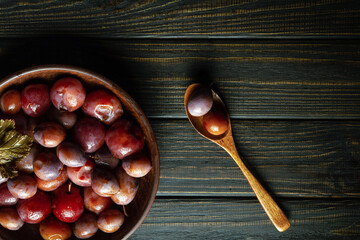 Pickled plums in a bowl and spoon on a vintage table. Free space for advertising.