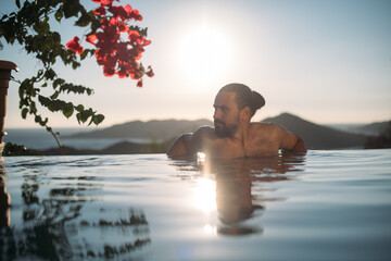 A young sexy man is relaxing in an open-air pool at sunset.