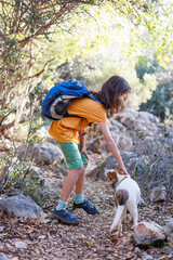 boy rests while trekking and plays with a dog.. A boy with a backpack plays on a mountain path with a dog. hiking with an animal and a child.