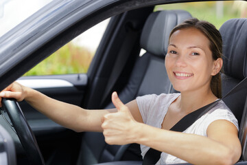 happy young woman in car with thumbs up