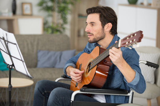 man playing guitar at home looking at music sheet