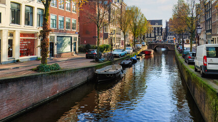 Fototapeta premium Famous Amsterdam city center canal with dutch brick buildings, trees , reflections and anchored boats in sunny autumn day. Nedherlands. 
