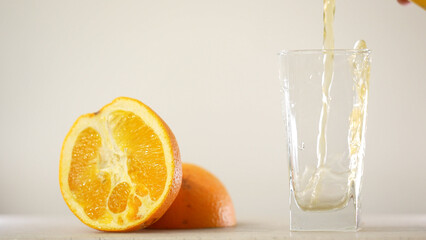 Detail Shot of Pouring Fresh Orange Juice into Glass. Appetizing orange juice swirls into a wave in a glass against the background of cut oranges.