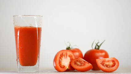 Delicious tomato juice is poured in jug next to tomatoes on the background 