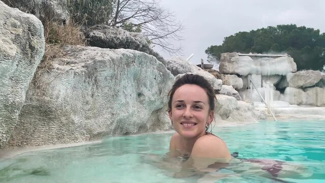 Healthy resort under the open air, pretty smiling woman relaxing in thermal hot water spring with sulphur vapours, antivirus, antifungal, anticancer and anti-inflammatory properties for human body