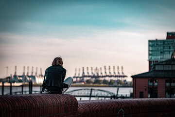 Fototapeta na wymiar Person sitting on a wall in the harbour of Hamburg, Germany