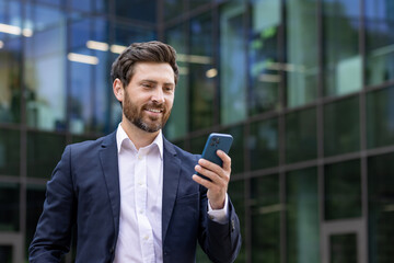 Confident bearded businessman using smartphone outside modern office building