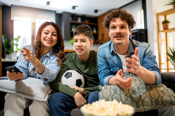 Latino family is watching football match and eating popcorn.They are cheering for their team.