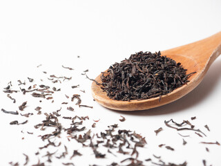 close-up of a wooden spoon with black than on a white background. Tea leaves are scattered around