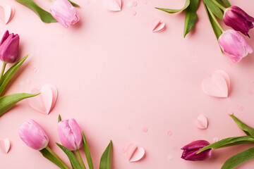 Cherished whispers: a delicate confession of the heart. Top view shot of pink and purple tulips, paper hearts and confetti on a pink background with space for tender words