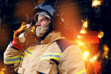 Portrait firefighter talking on radio walkie talkie with colleagues background wooden house in fire - obrazy, fototapety, plakaty