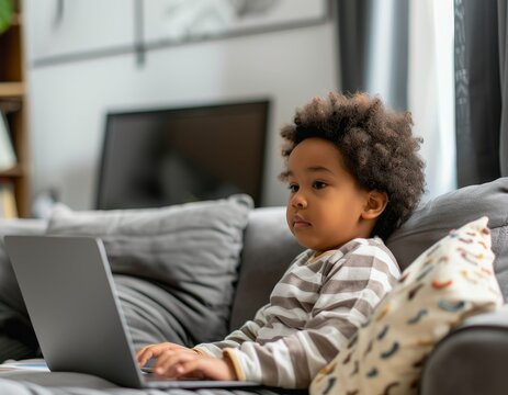 Child sitting on a couch, attentively using a laptop for online classes.