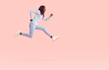 Fototapeta na wymiar Funny afican american girl wearing casual clothes jumping high isolated on a pink background. Portrait of a happy young excited woman in a hurry having fun in studio. People emotions concept.