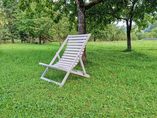 White wooden chaise lounge on a clearing in the garden on a summer day. Lounger for sunbathing and relaxation