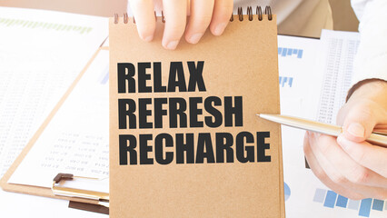 Text RELAX REFRESH RECHARGE on brown paper notepad in businessman hands on the table with diagram....