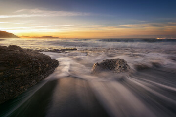 Sunset on Azkorri beach, Getxo with the wakes of the waves between the rocks in the foreground