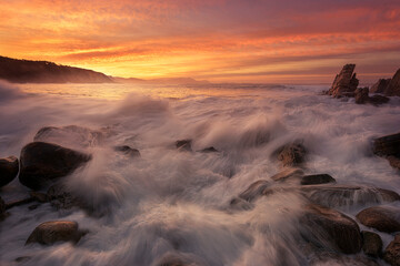 Sunset on Azkorri beach, Getxo with the wakes of the waves between the rocks in the foreground