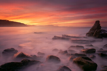 Sunset on Azkorri beach, Getxo with the wakes of the waves between the rocks in the foreground